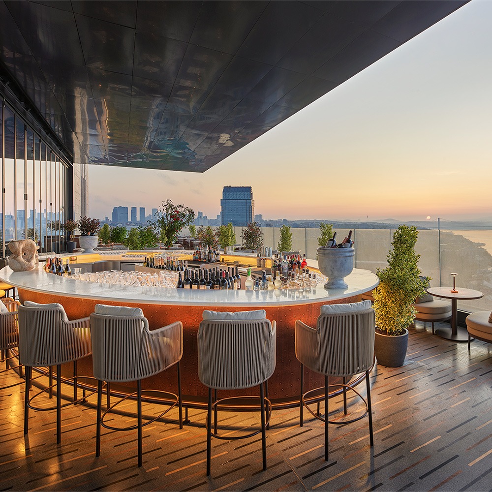 Rooftop bar with elegant seating, city skyline view, and sunset in the background. Perfect nightlife ambiance.