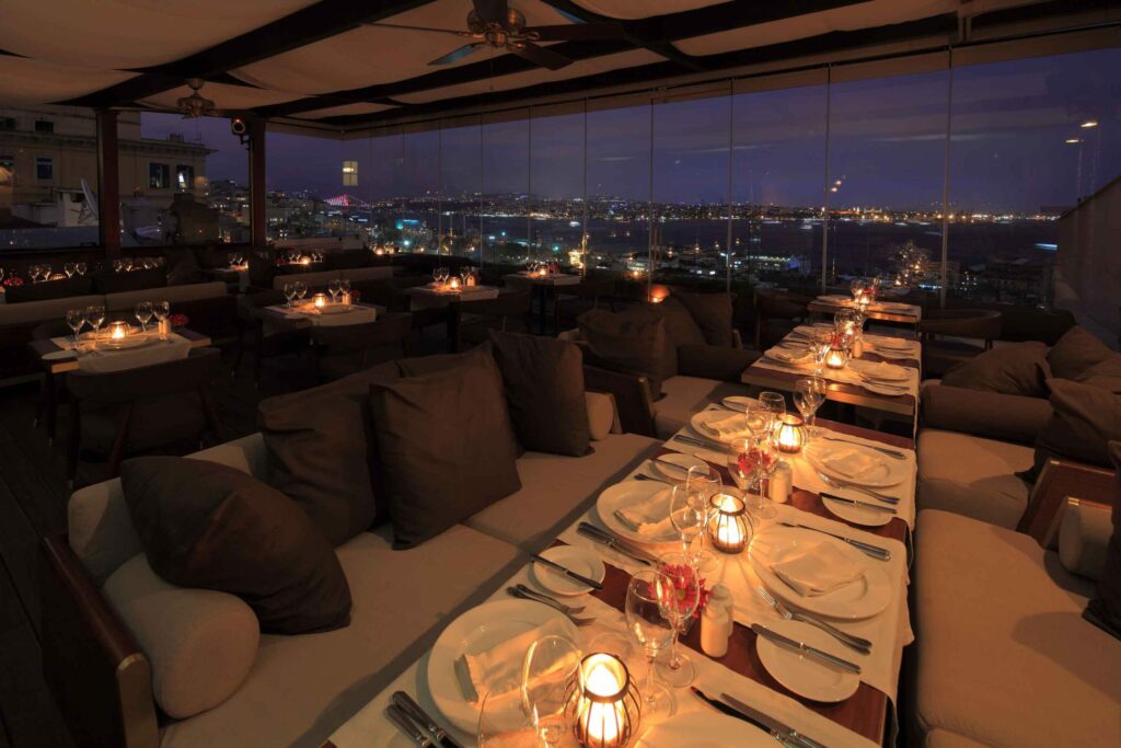 Romantic rooftop restaurant with elegant table setup overlooking city lights at night.