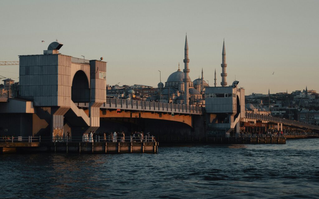 Galata Bridge at sunset with a mosque in the background, Istanbul's skyline over water.