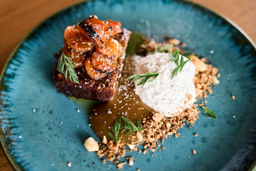 Gourmet dessert with roasted caramelized fruits, whipped cream, and nut crumble on an elegant blue plate.
