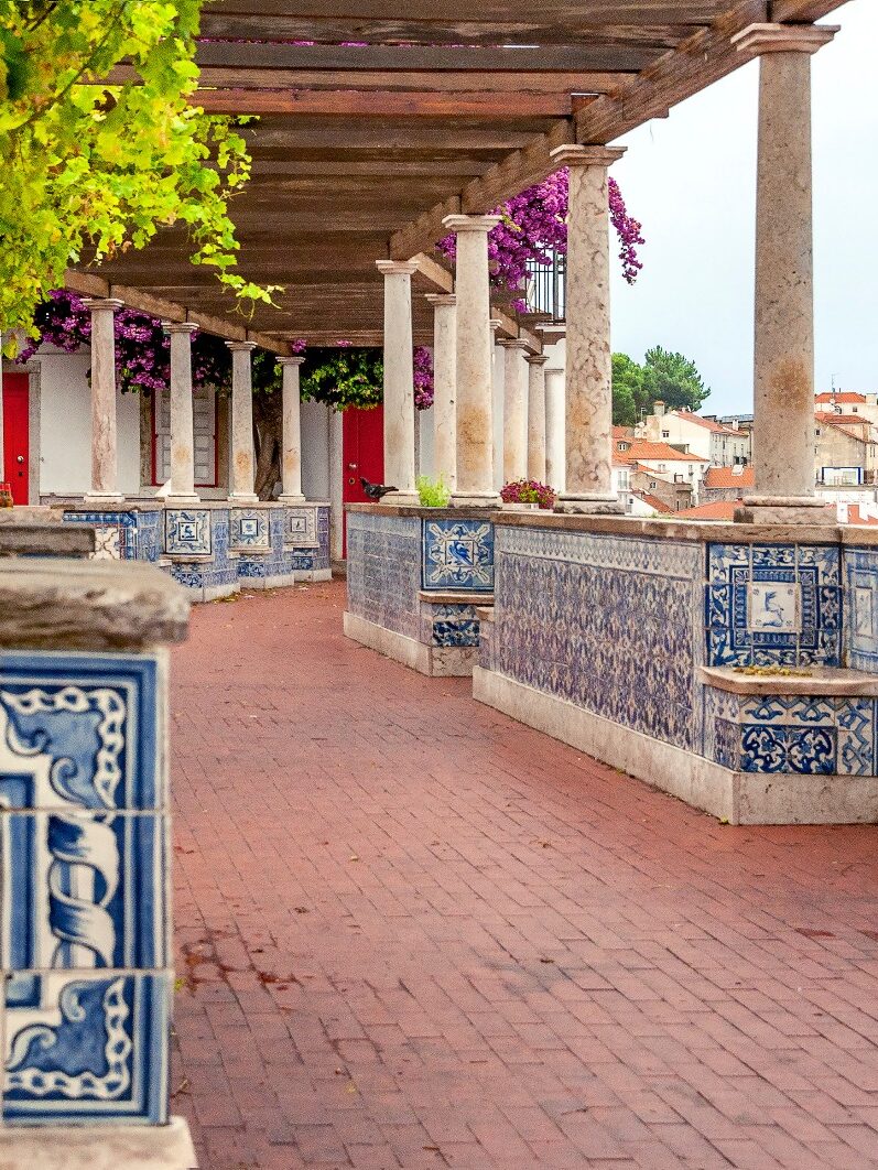 Scenic terrace with blue tiles and vines overlooking Lisbon cityscape.