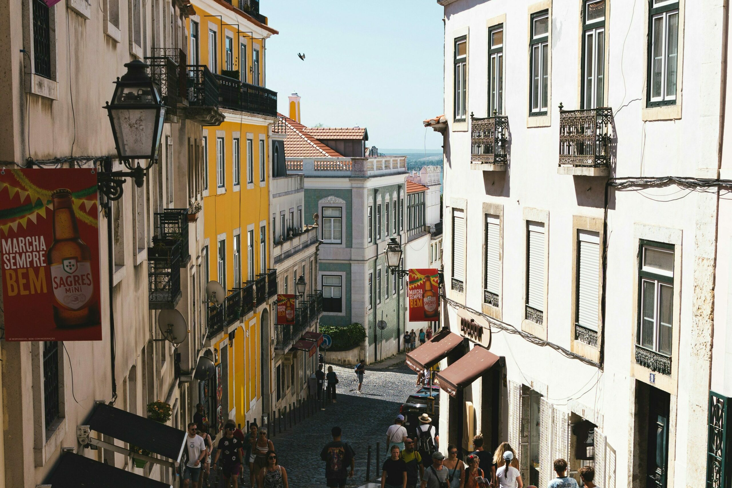 Colorful Lisbon street with people walking on cobblestones between historic buildings under a clear blue sky.