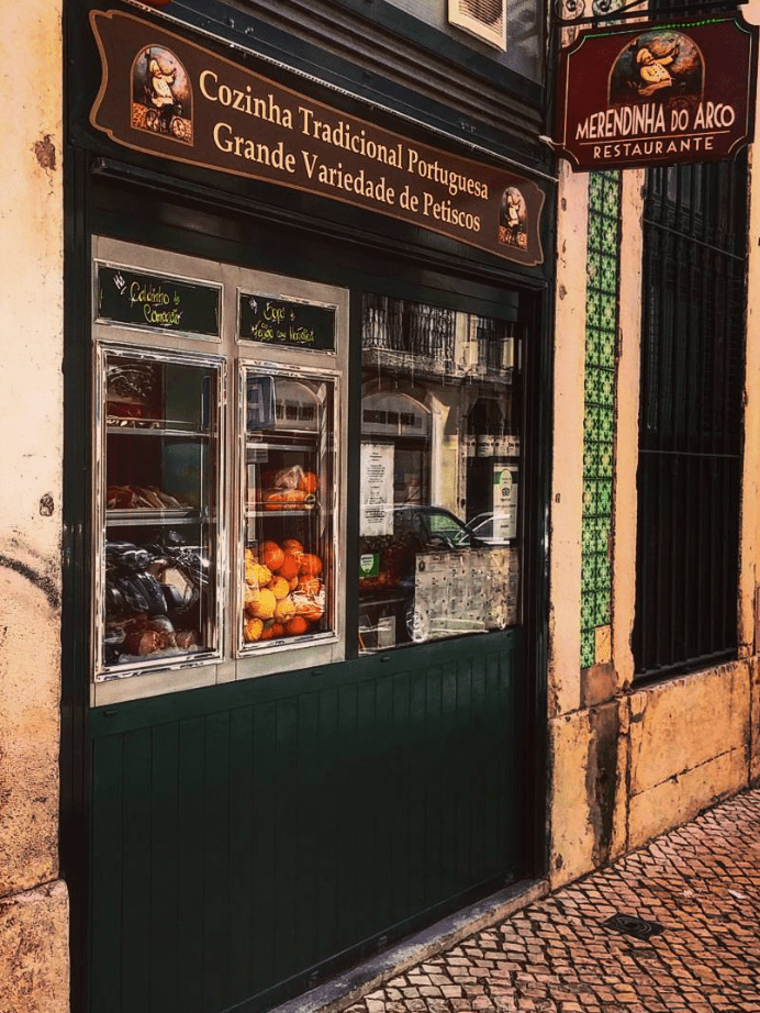 Traditional Portuguese restaurant with fruit display, featuring green tiled walls and menu board outside.