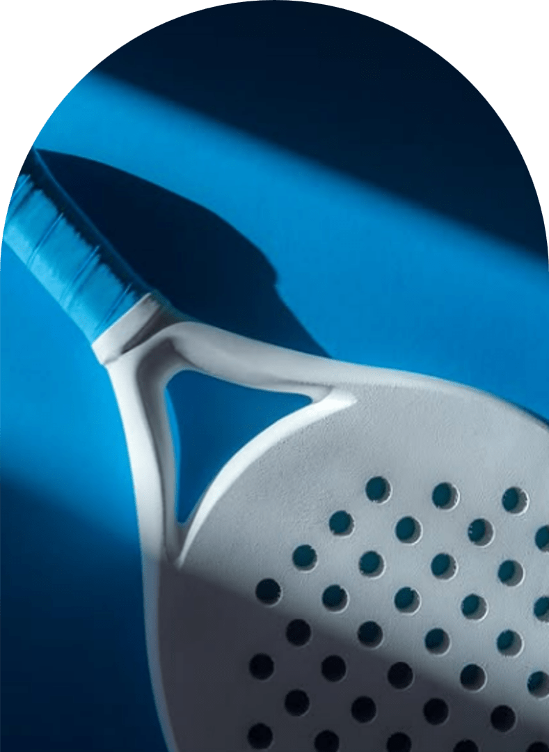 Close-up of a white padel racket with blue grip on a blue background, angled under dramatic shadow.