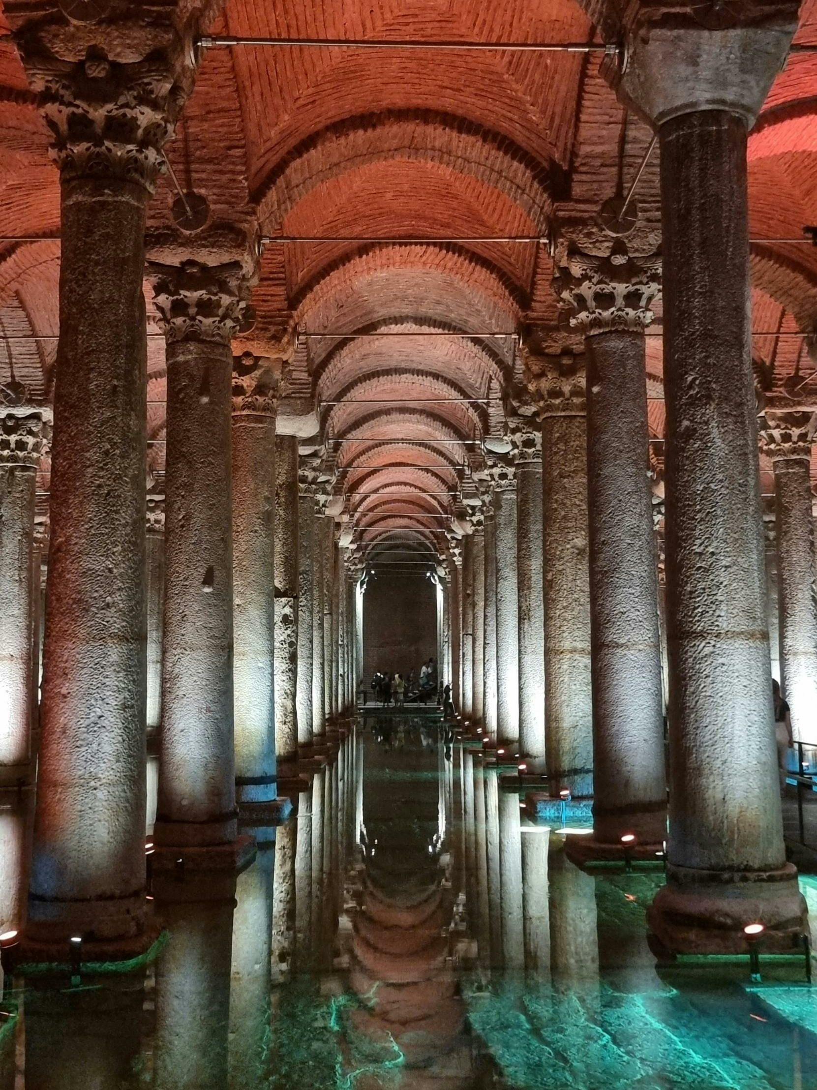 Ancient underground cistern with illuminated arches and columns, reflecting in the water below.