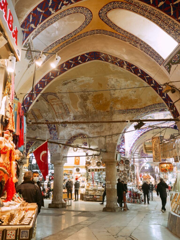 Bustling interior of a traditional Turkish bazaar with colorful goods and shoppers under ornate ceilings.