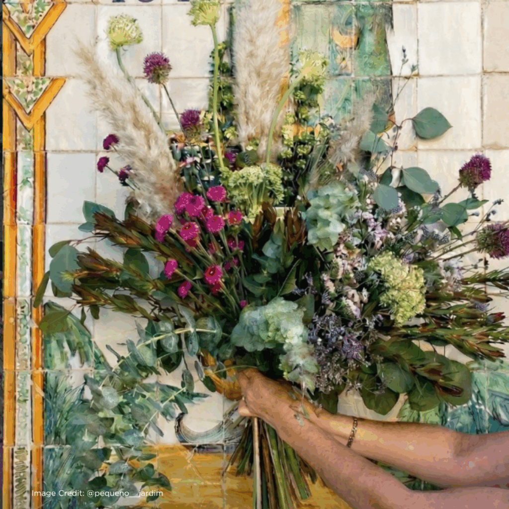 Vibrant floral bouquet held against a colorful tile backdrop, showcasing various blooms and greenery.