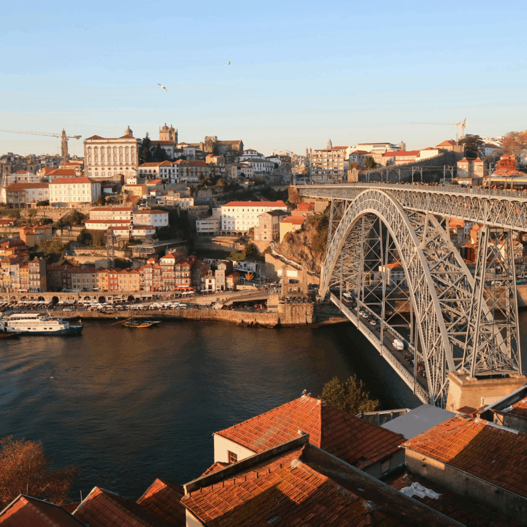 Scenic view of Porto with the iconic Dom Luís I Bridge spanning the Douro River at sunset. Historic buildings line the shore.