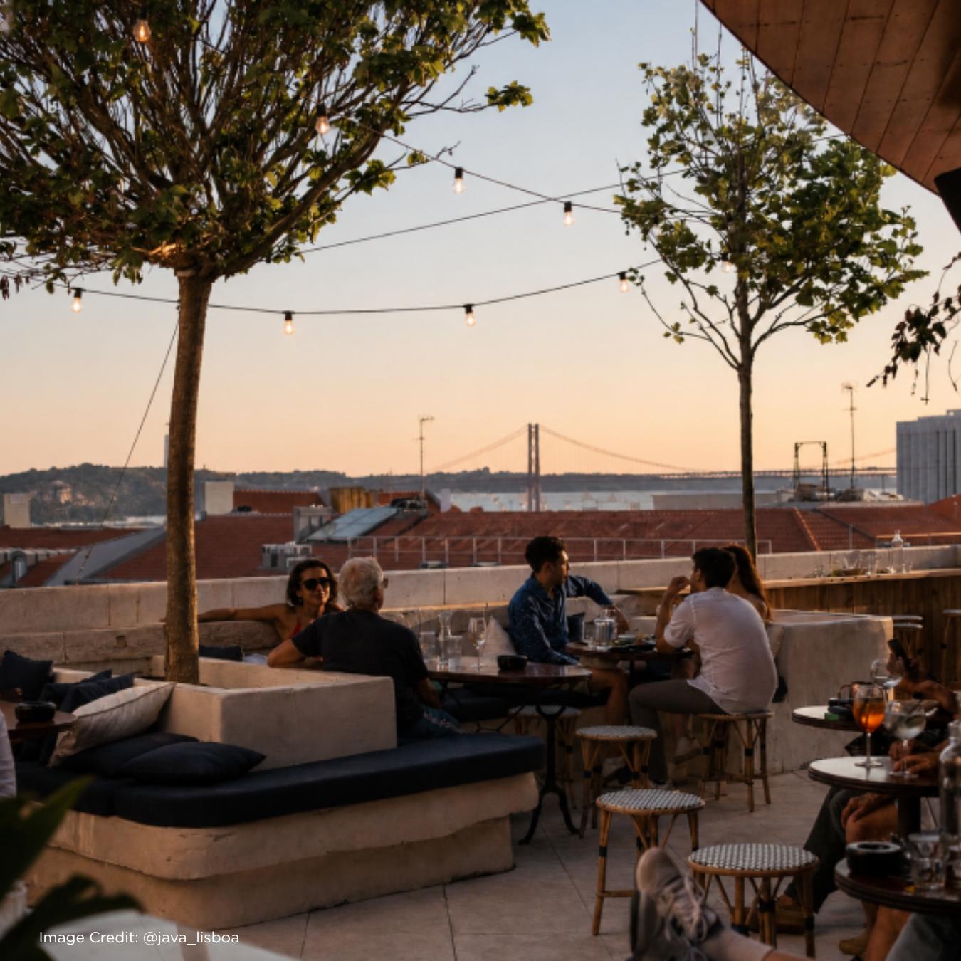 Sunset view from a rooftop bar in Lisbon, with patrons enjoying drinks and conversation under string lights.
