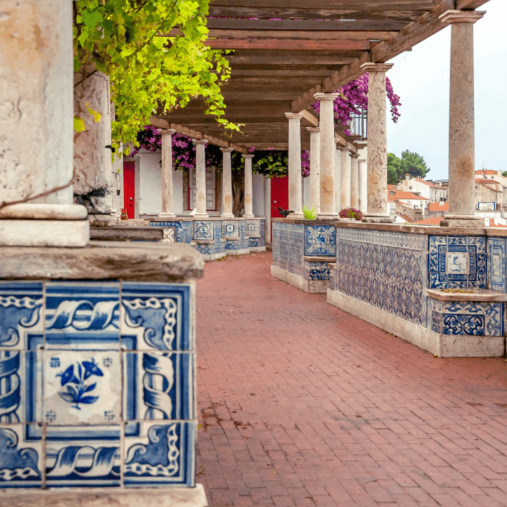 Charming colonnade with blue tiles, vibrant flowers, and rustic columns, creating a picturesque architectural scene.