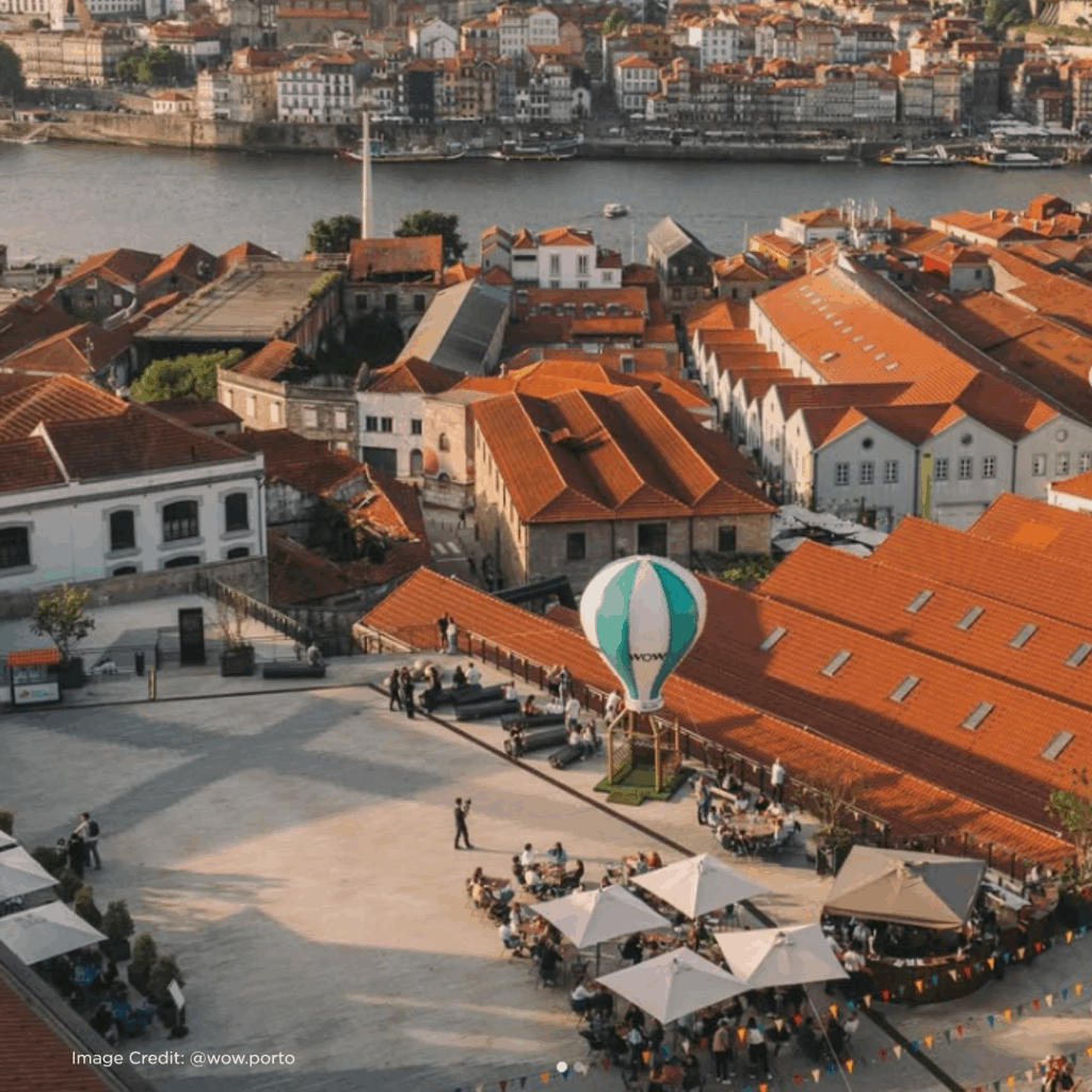 Aerial view of Porto's vibrant waterfront, featuring red-roofed buildings, a hot air balloon, and lively outdoor seating.