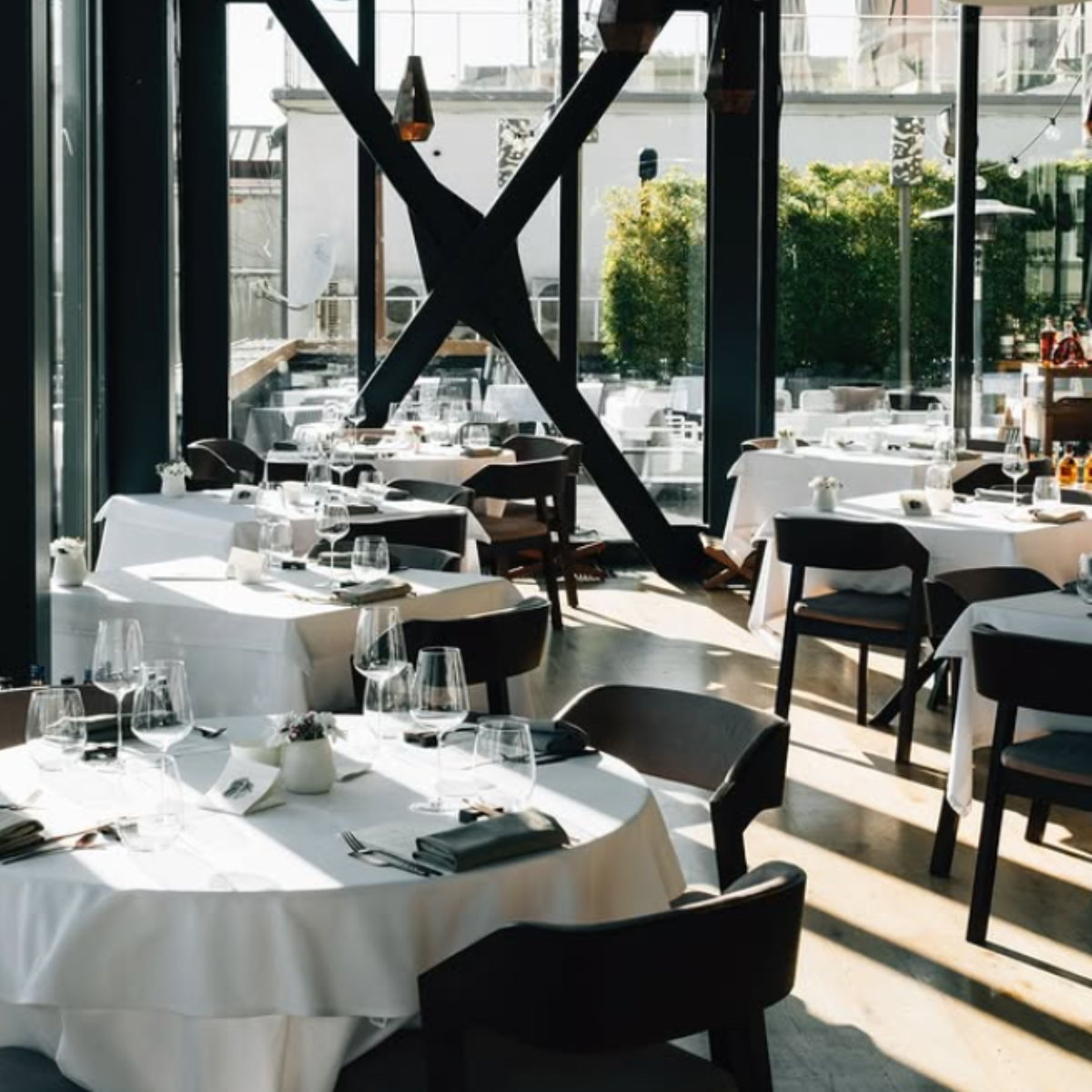 Modern restaurant interior with elegant tables, glass windows, and a bright, inviting atmosphere. Perfect for dining.