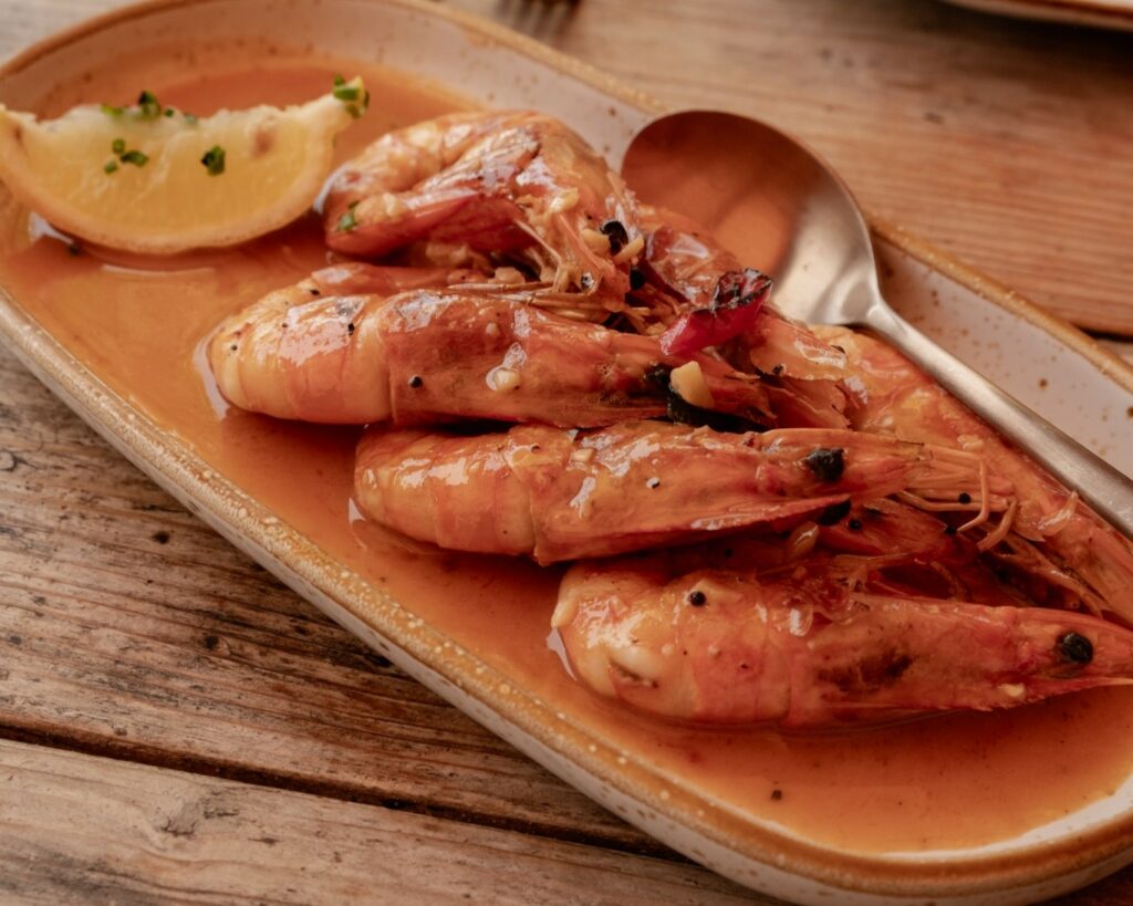 Deliciously cooked shrimp in a savory sauce, garnished with a lemon wedge, served on a rustic wooden table.