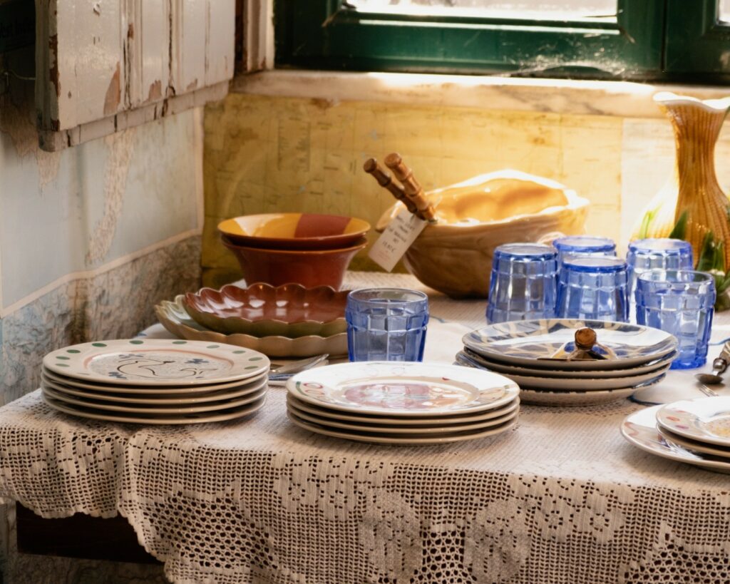 A cozy table setting with colorful handmade plates, bowls, and blue glassware, adorned with a lace tablecloth.