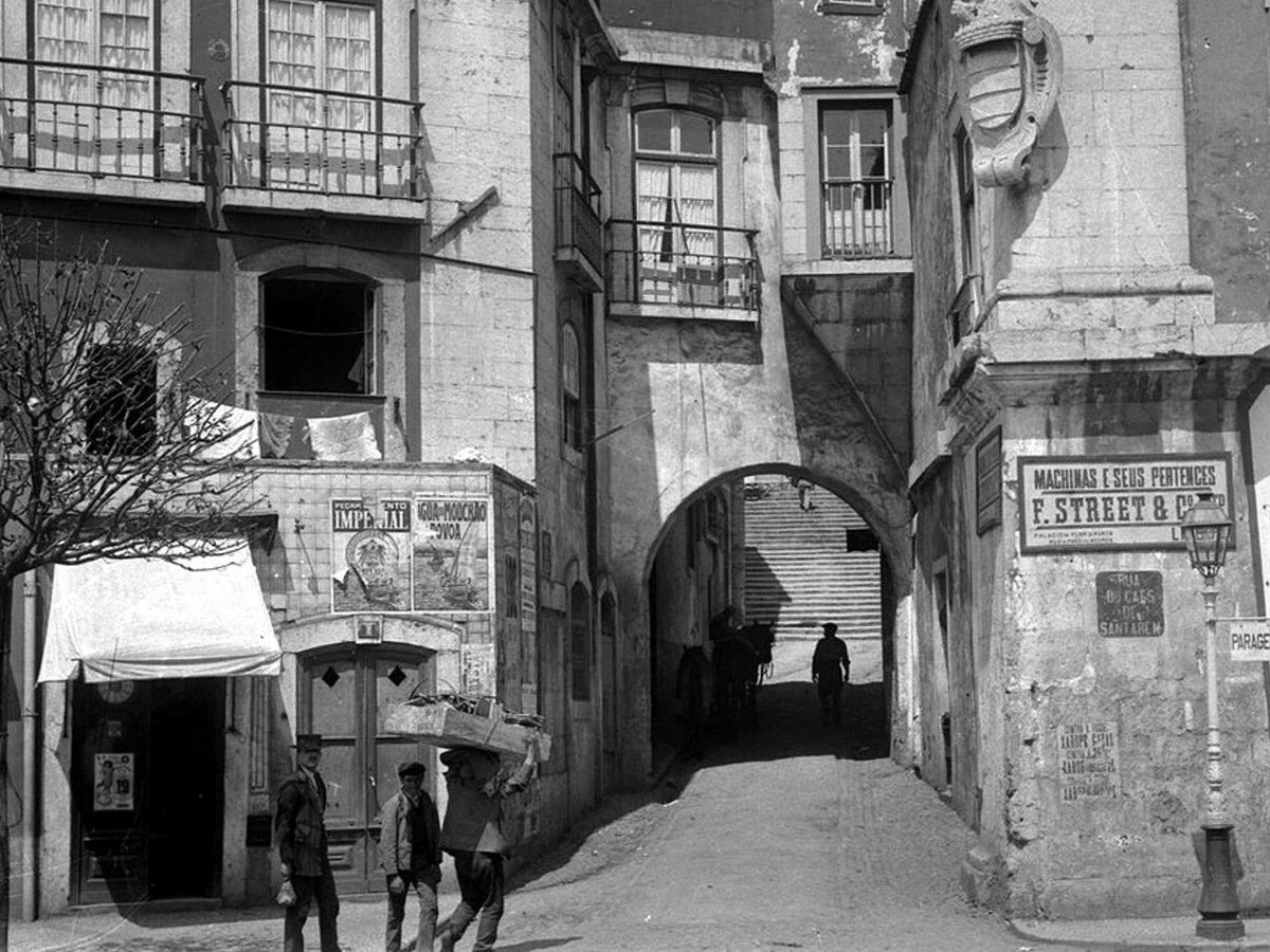 Historic street view featuring archway, vintage buildings, and pedestrians in black and white. Capture of urban life.