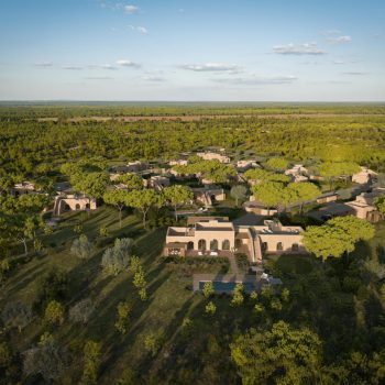 Aerial view of a luxury resort nestled in lush greenery and natural landscape under a clear blue sky.