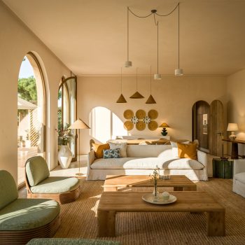 Bright modern living room with natural light, chic wicker furniture, and green views through arched windows.