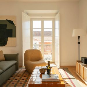 Sunlit living room with sofa, lounge chair, and balcony doors bringing natural light into the space.