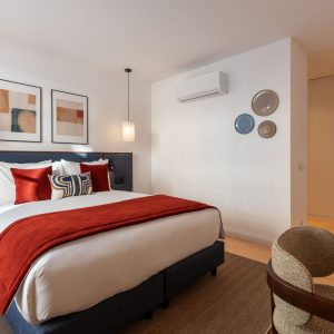 Contemporary bedroom with red accent bedding, upholstered headboard, and minimalist artwork creating a warm atmosphere.