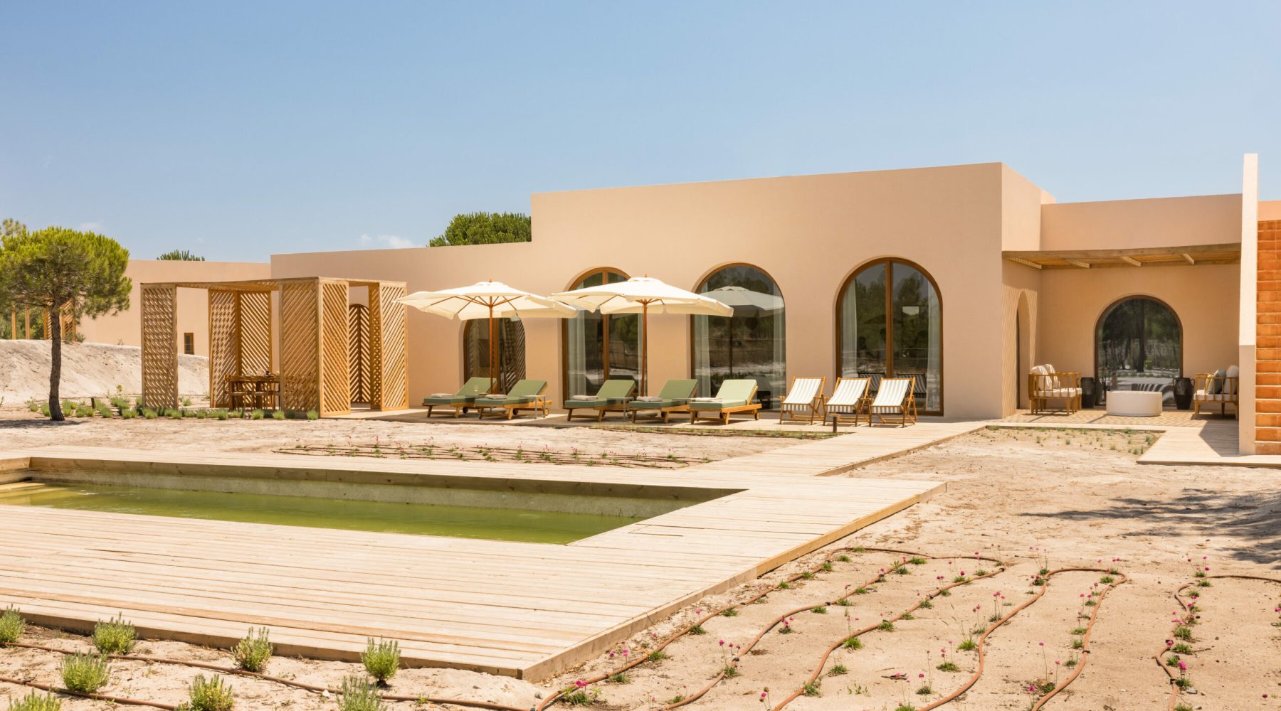 Ando Living Comporta Villas. Modern vacation home with pool, sun loungers, and shaded seating area in a serene outdoor setting. Perfect for relaxing.