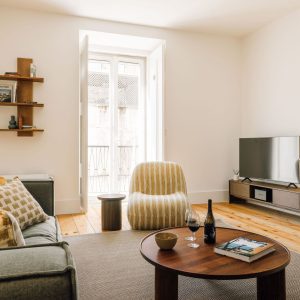 Bright living room with sofa, armchair, wooden coffee table, and balcony doors bringing in natural light.