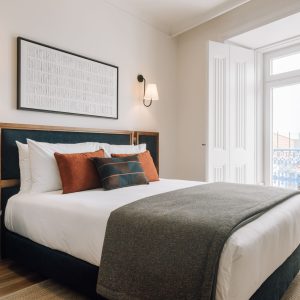 Elegant bedroom with upholstered headboard, warm wooden accents, and balcony doors letting in natural light.