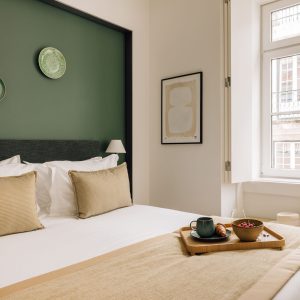 Cozy bedroom with green accent wall, stylish decor, and breakfast tray on bed near a bright window.