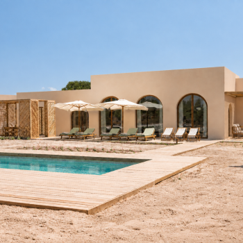 Modern villa with a pool, wooden deck, and shaded lounge chairs in a serene outdoor setting under a clear blue sky.