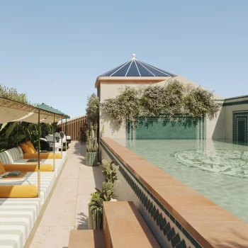 Luxurious rooftop pool with sun loungers and poolside cabanas, surrounded by lush greenery under a clear sky.