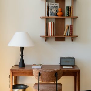 Minimalist study nook with wooden desk, vintage shelf, modern lamp, and speaker, accented with books and decor items.