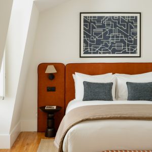 Modern bedroom with geometric artwork, orange headboard, and plush bedding. Cozy ambiance with natural light.