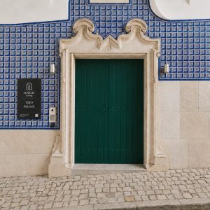 Ando Living Tejo Palace. Green door on blue-tiled wall of Tejo Palace, featuring elegant architectural details and a nearby sign for Ando Living.